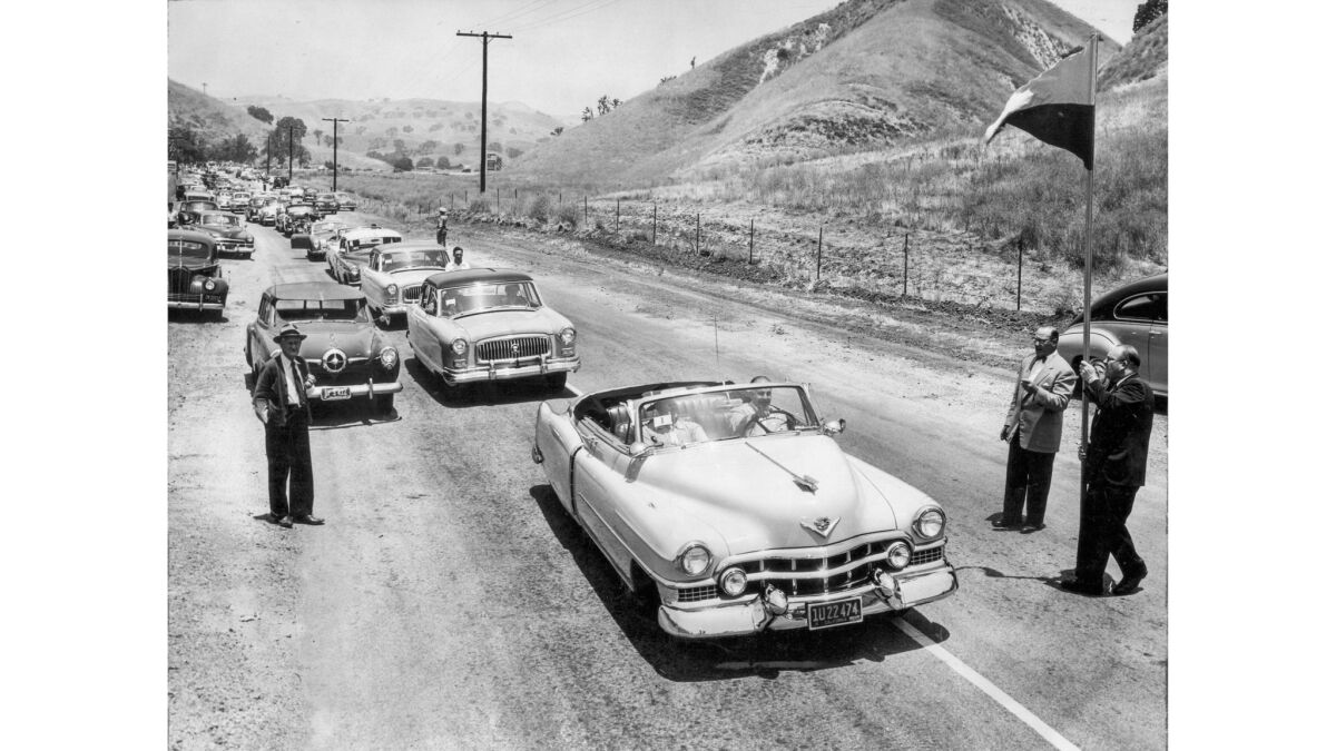 Cars line up on Malibu Canyon Road as a man holds a flag on a tall pole