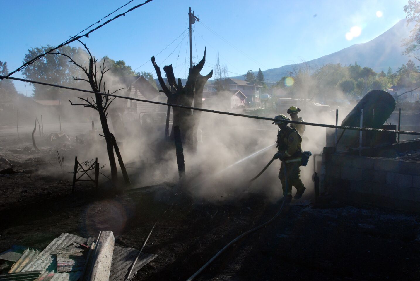 Firefighters hose down the smoldering remains of a home in Weed, Calif., on Tuesday.