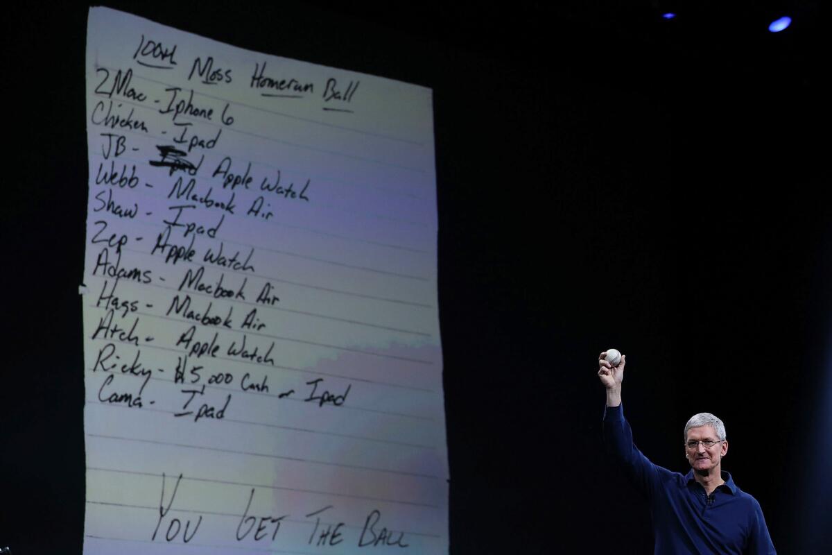 Apple CEO Tim Cook holds up the baseball coveted by Brandon Moss in front of a projected image of the ransom note for it sent by Moss' teammates.