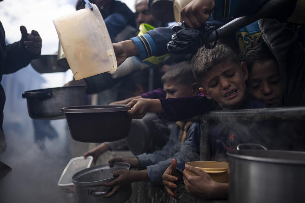 Palestinian children hold pots and pans in a line for a meal in Rafah, Gaza Strip. 