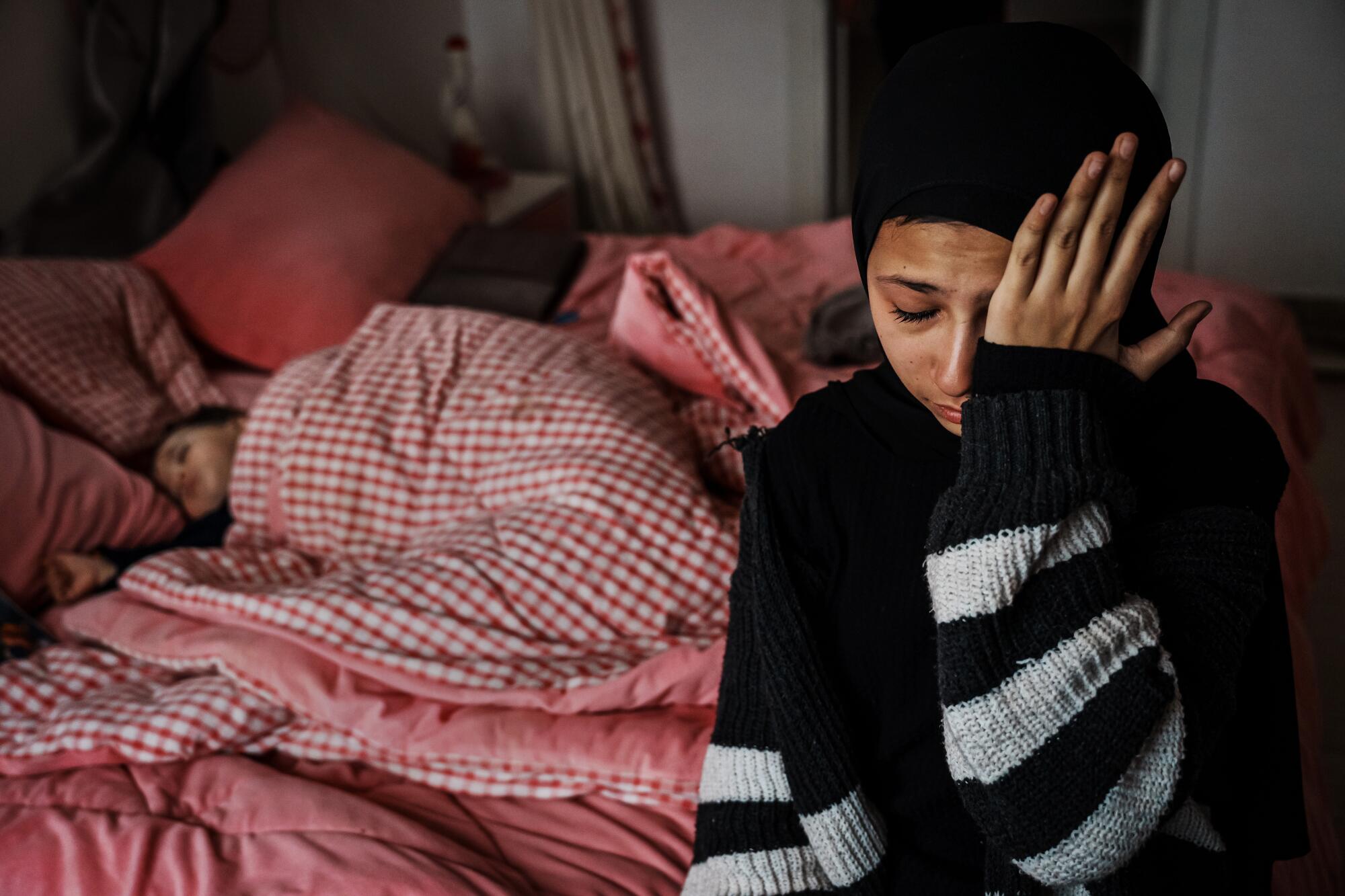 Layan Jalamneh cries while sitting near people sleeping in blankets.
