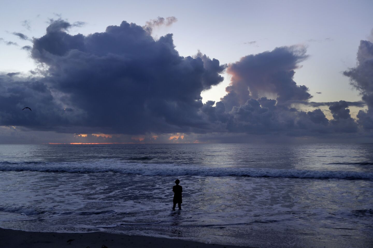 A woman stands in the surf and looks at the clouds at sunrise as Hurricane Florence approaches in Wrightsville Beach, N.C., Wednesday, Sept. 12, 2018.