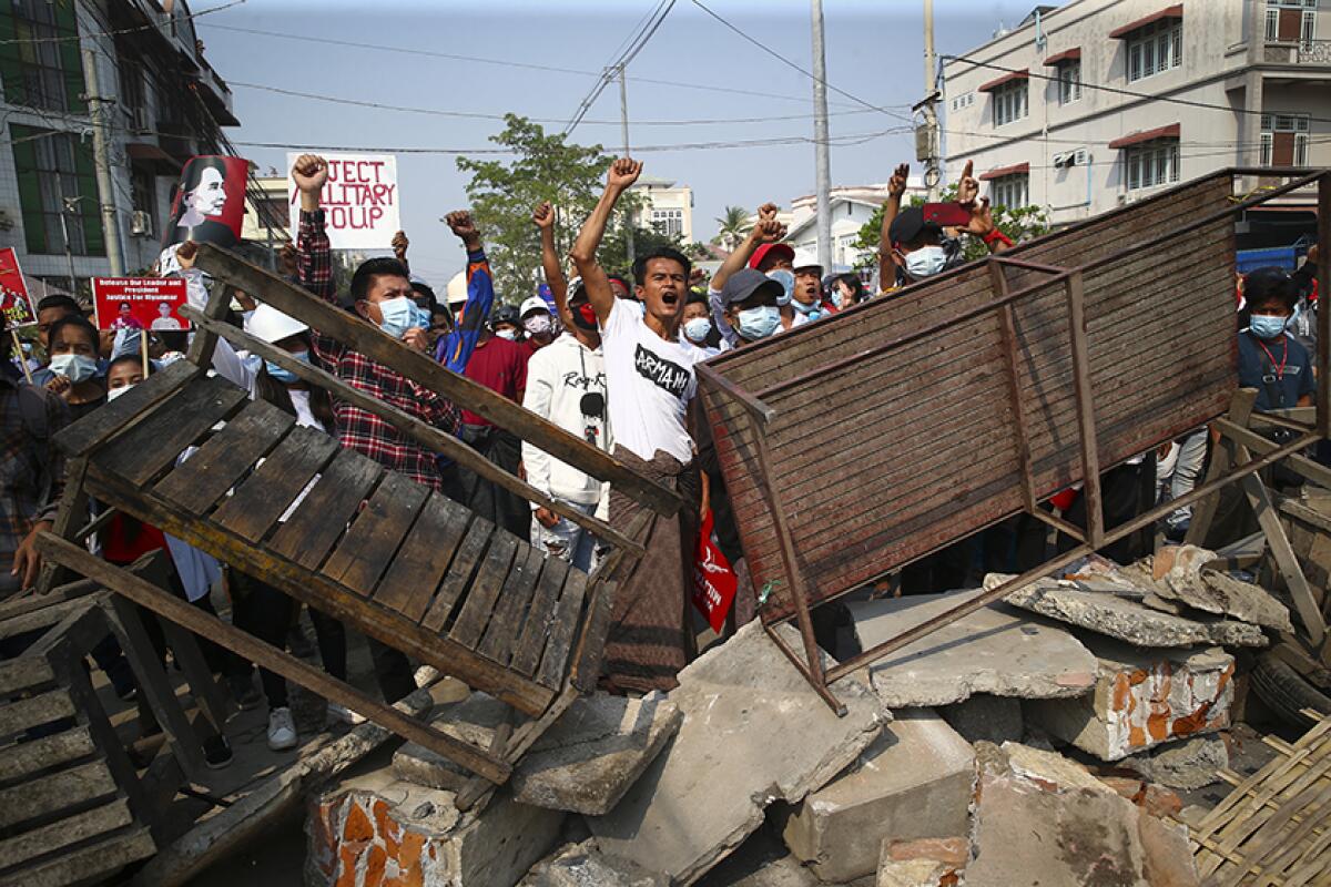 People lift their fists and yell from behind a barricade of broken concrete and benches.