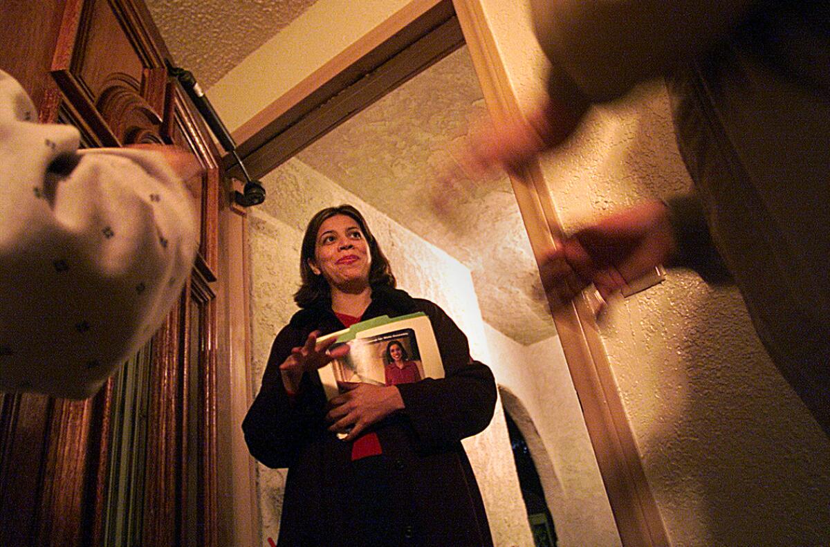 A woman stands in an open doorway holding printed matter.