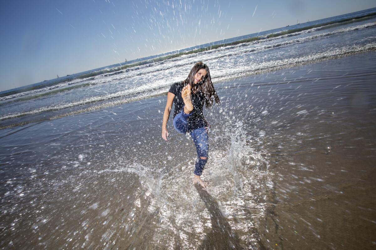A woman splashes water up with her foot at the ocean's edge