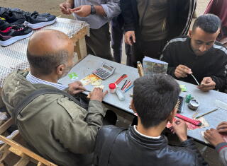 People sit at a table and work on repairing shekel notes.