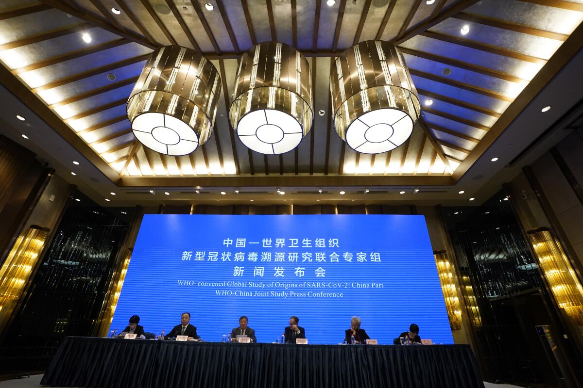 Six panelists sit in front of a screen at the WHO-China joint study press conference.