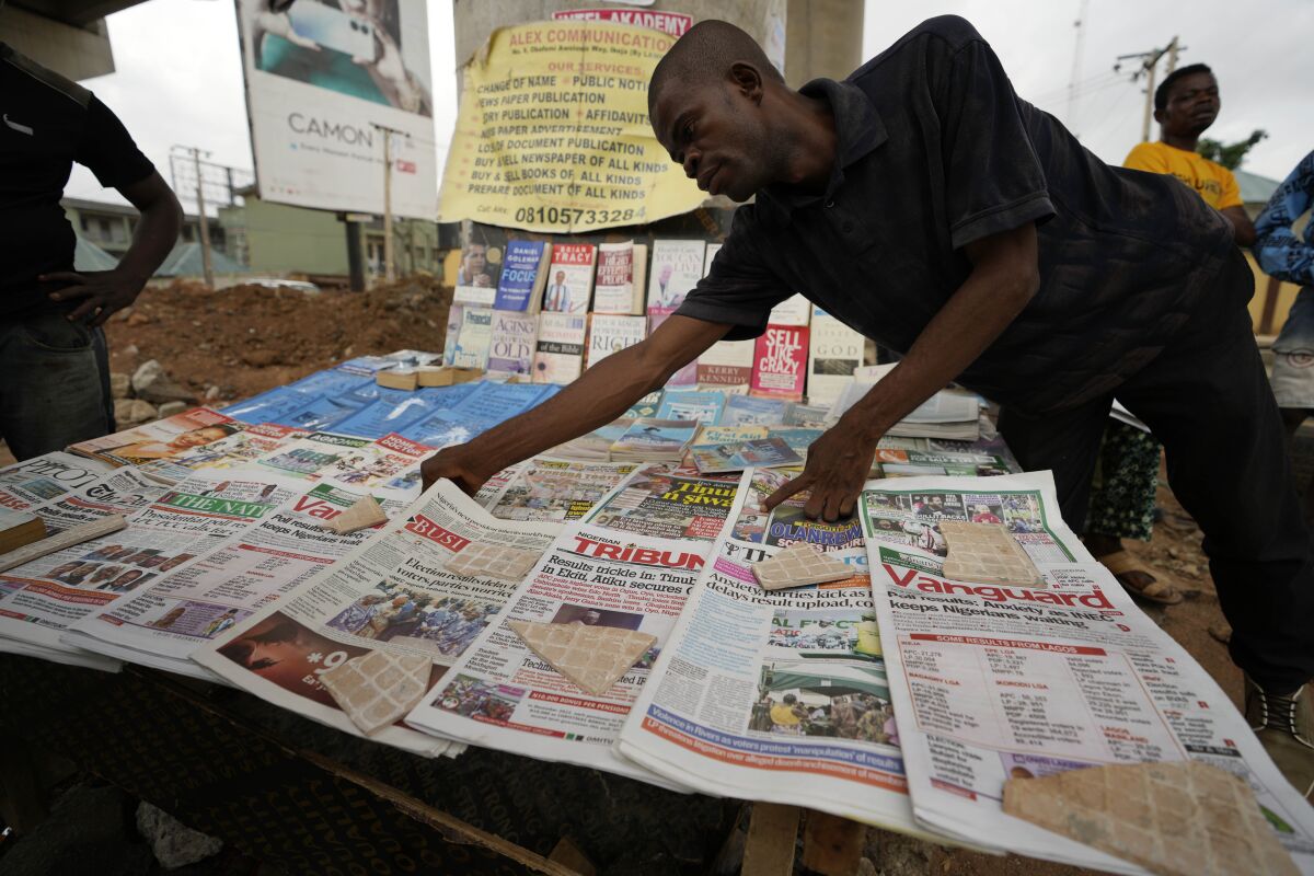 A man in dark clothing arranges newspapers at a street newsstand