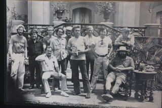 A black and white photo of 11 men dressed in 1960s clothes.