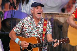 Jimmy Buffett performs with a guitar on a stage
