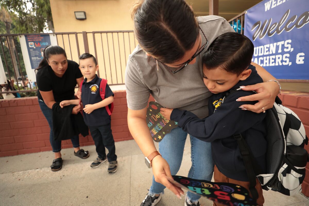 A young student hugs his parent outside a school.