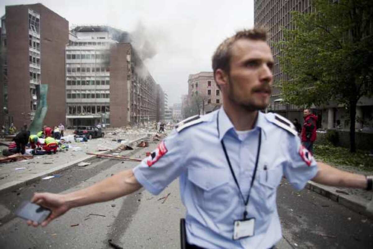 An official attempts to clear away spectators from buildings in the centre of Oslo following an explosion in July 2011.