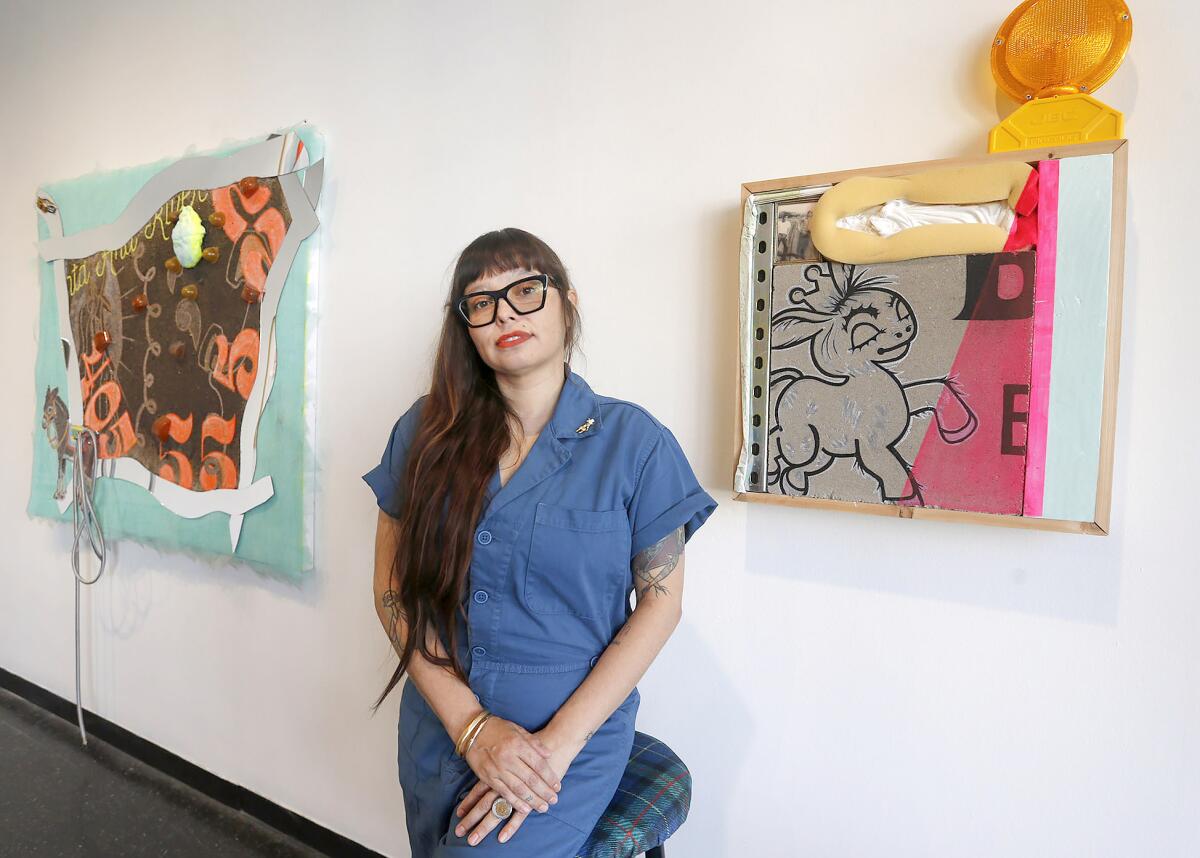 Santa Ana artist Lorena Ochoa stands with two of their signature pieces at "Se Busca." 