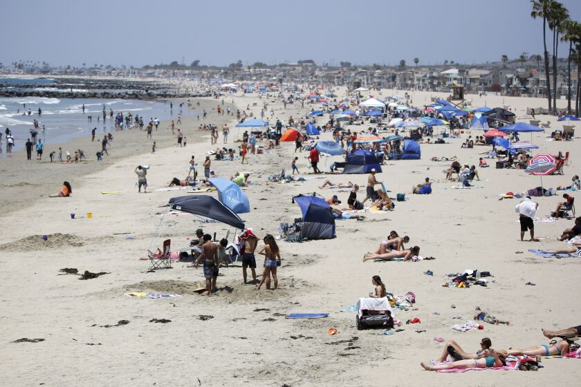 Beach goers practice social distancing while sunbathing near the Newport Pier in Newport Beach on Saturday, May 23, 2020.