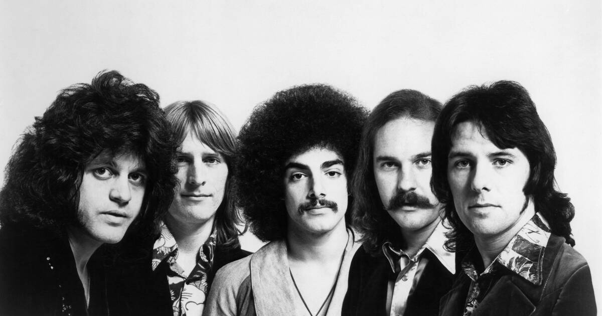 A black and white photo of Journey's founding members in '70s-style attire and hairdos, looking forward