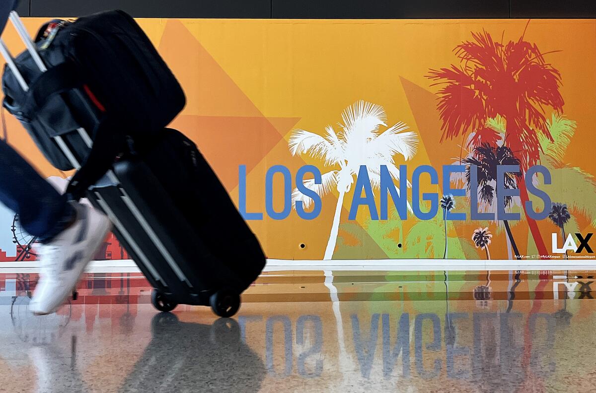 An orange wall sign reads "Los Angeles" as a foot and a rolling suitcase are about o step out of the frame to the left.
