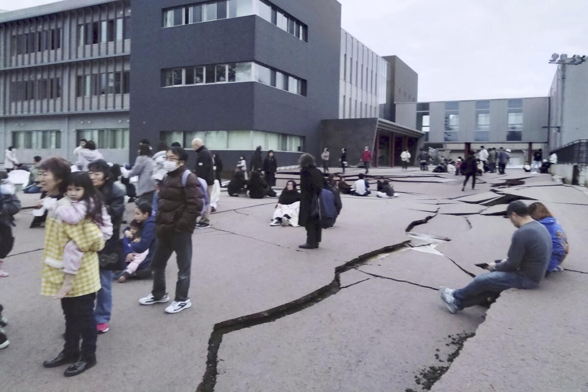 People stand or sit near cracks on the ground in Japan following an earthquake. 