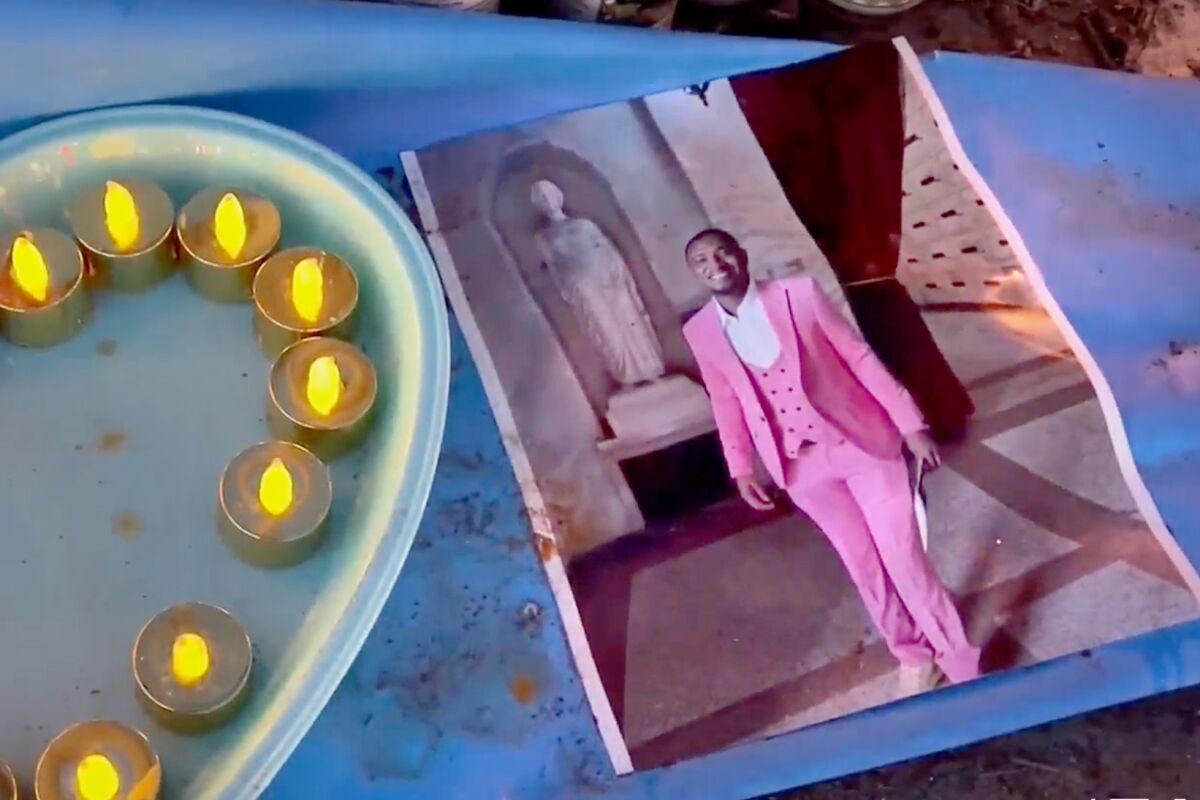 A photo of a smiling man in a pink suit, right, lies next to votive candles on a tray