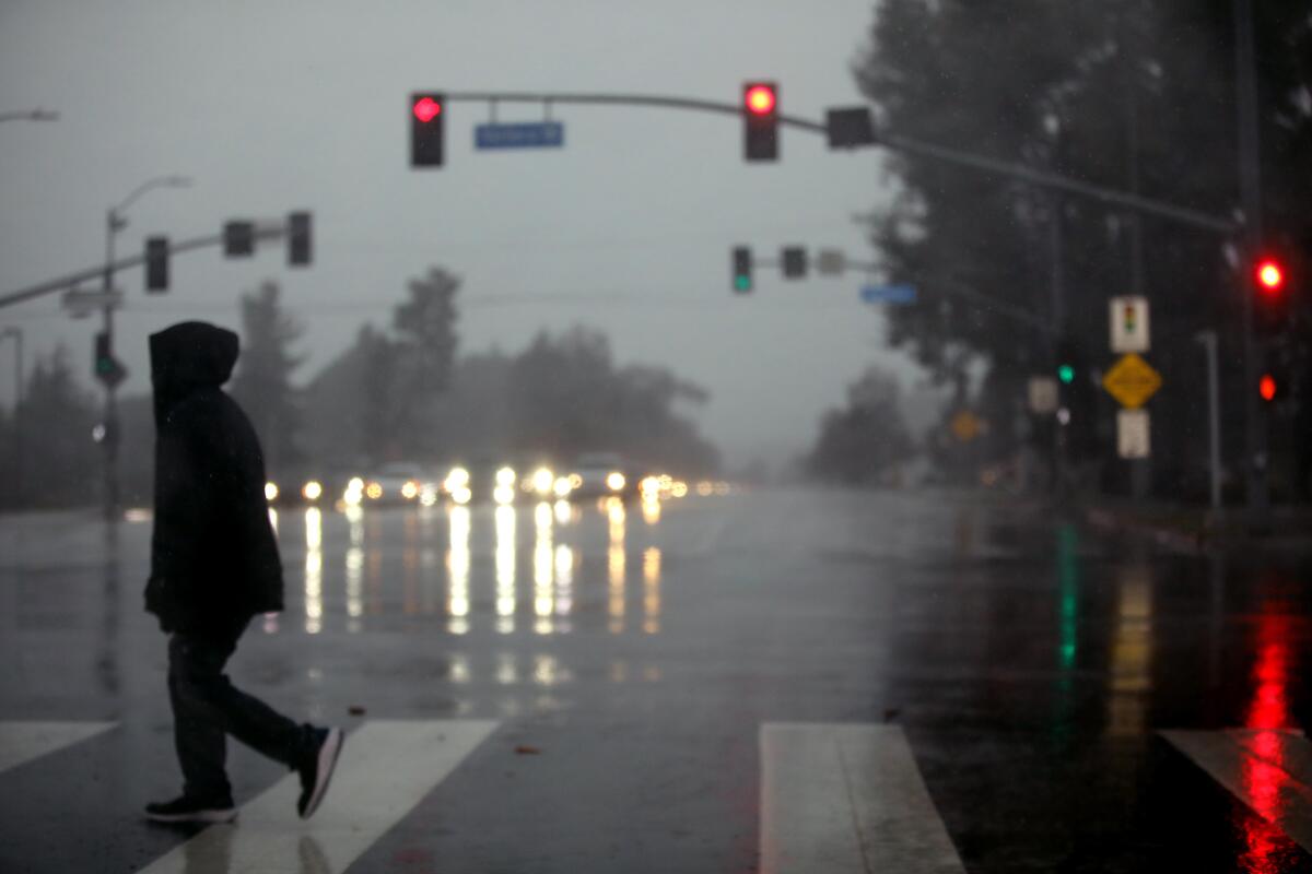A pedestrian make his way through the rain along Victory Boulevard in Encino.