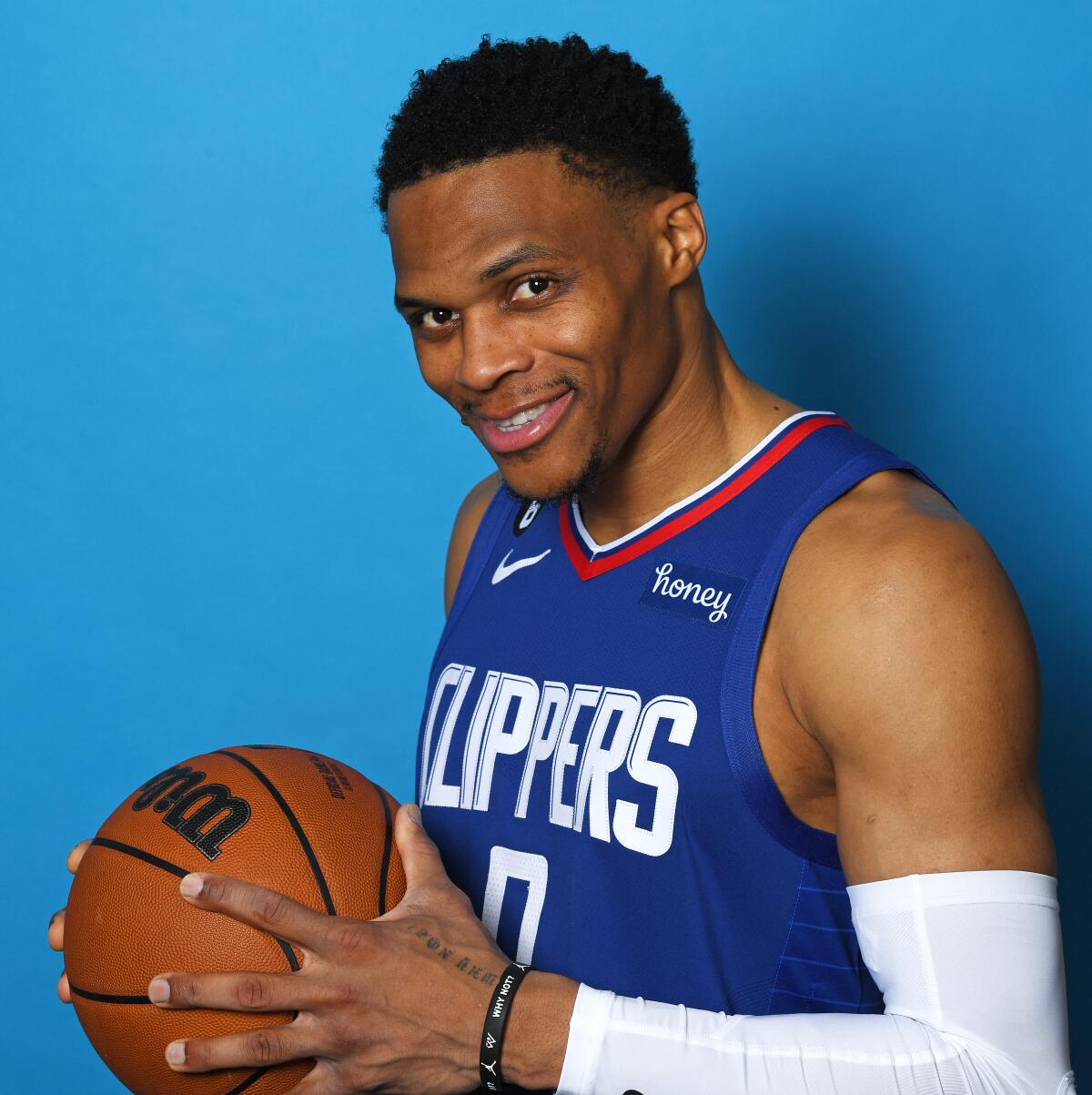 Russell Westbrook smiles and holds a basketball in a portrait.