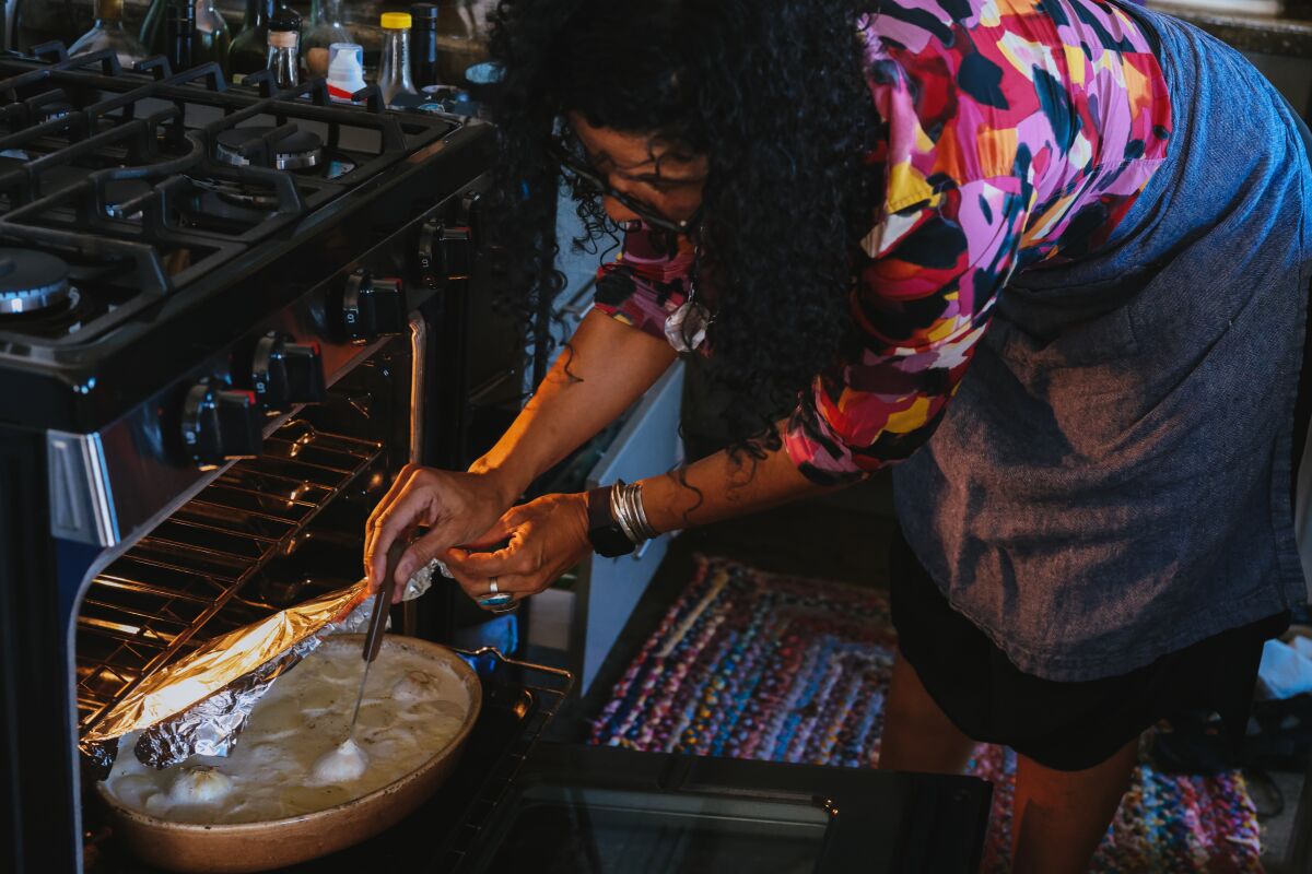 A woman leans over to stir a dish in the oven. 