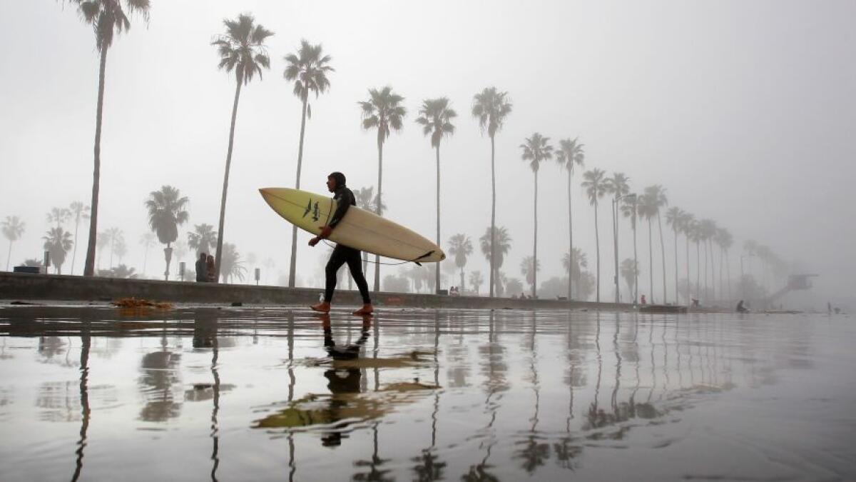 Gil Vargas gets out of the water after surfing at La Jolla Shores as thick fog envelopes the coast Sunday morning.