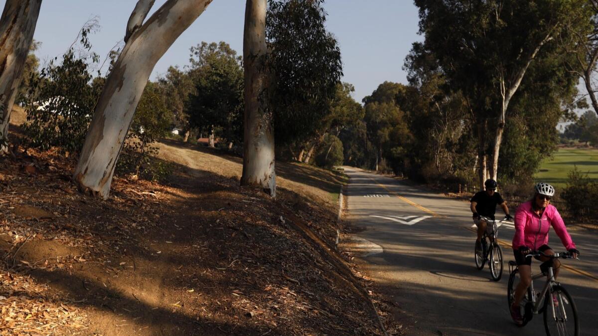 Bicyclists ride past the start of a path, left, along Paseo Del Campo that leads on a short hike through Palos Verdes Estates.