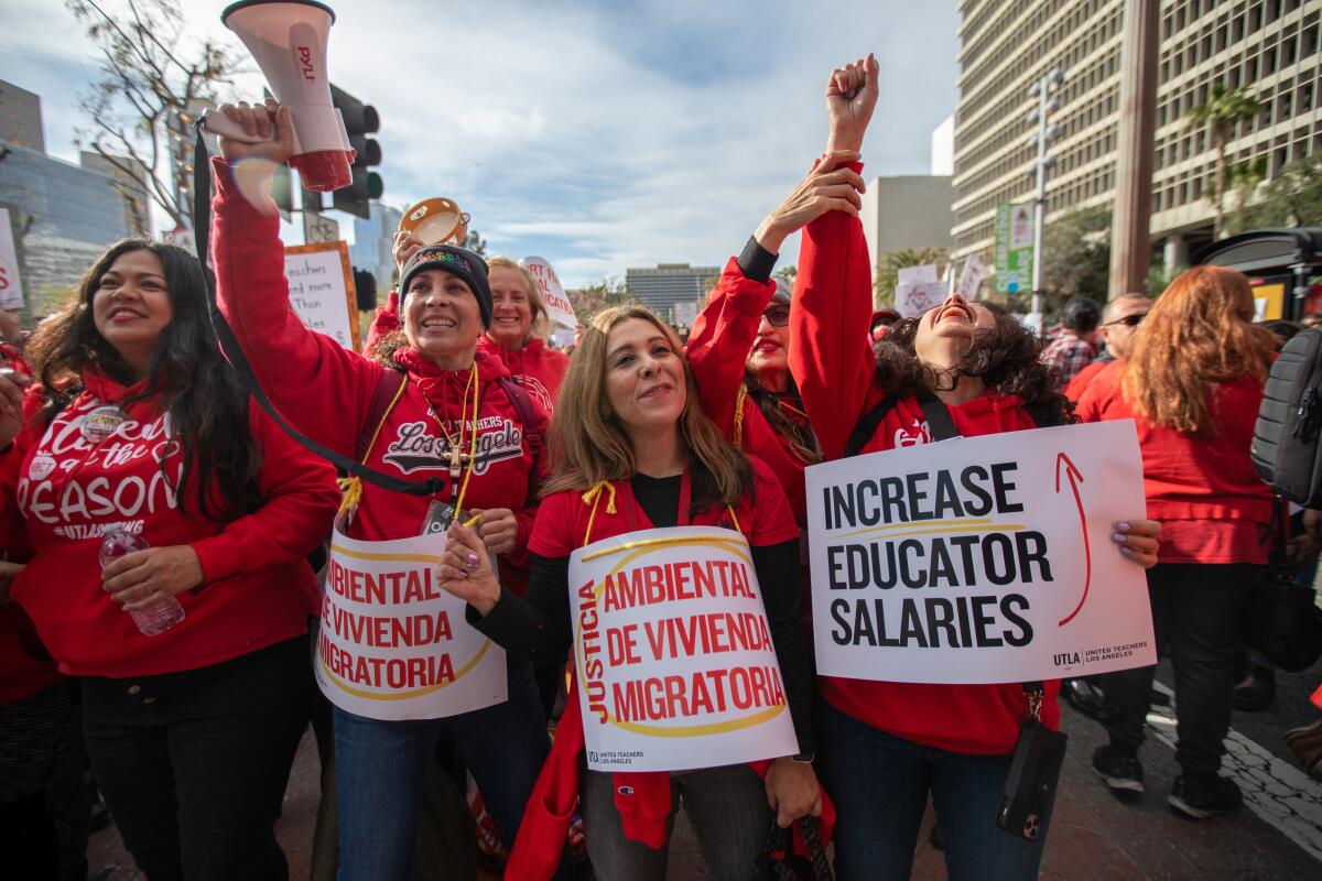 Women wearing red sweaters hold signs that advocate for increased salaries for school workers