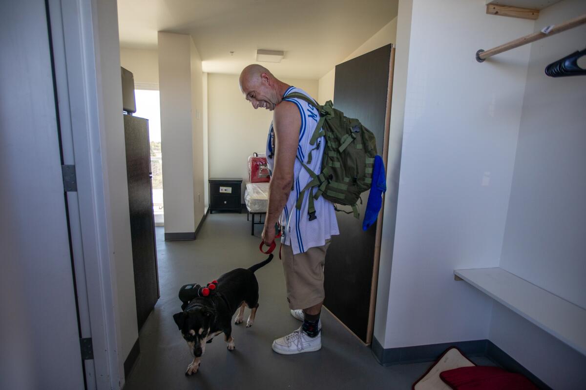 William Escribano, wearing a backpack, walks his dog into their apartment.