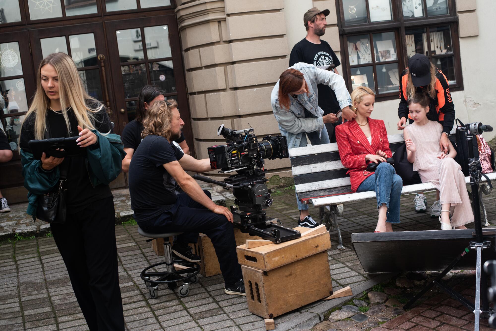 A cameraman sits next to a group of actors and others between takes