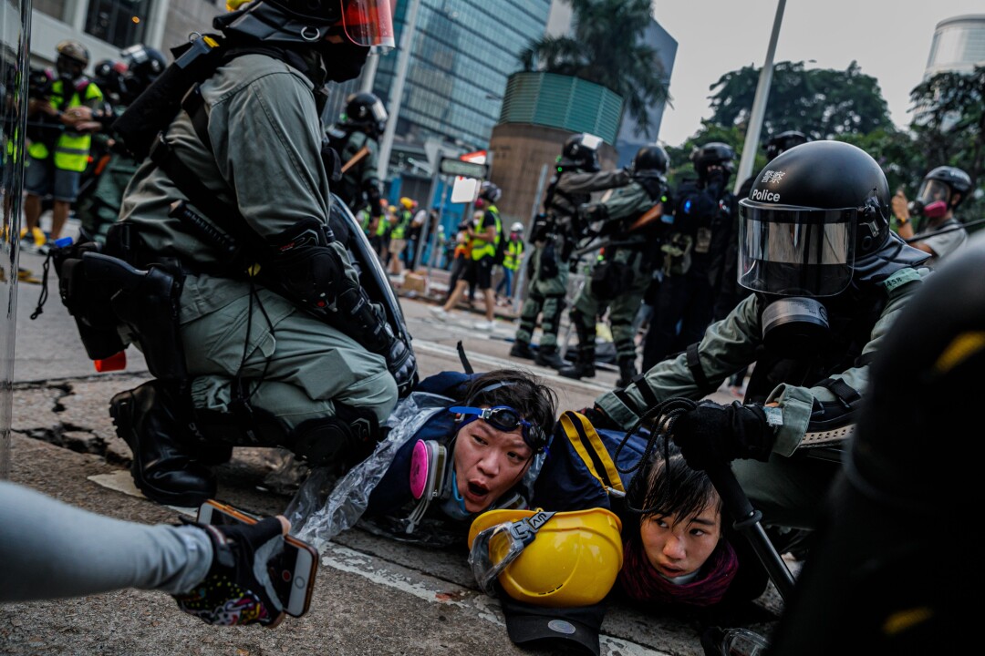 Two protesters are pinned down by police in riot gear