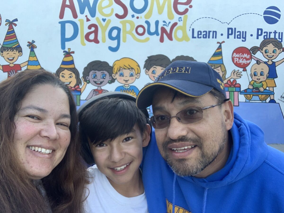 Kay Osorio with her son and husband outside a sign for the children's play destination.