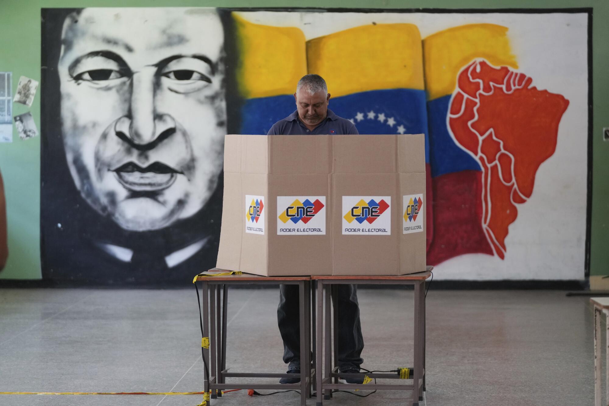 Un votante elige a su candidato frente a un mural del fallecido presidente venezolano 