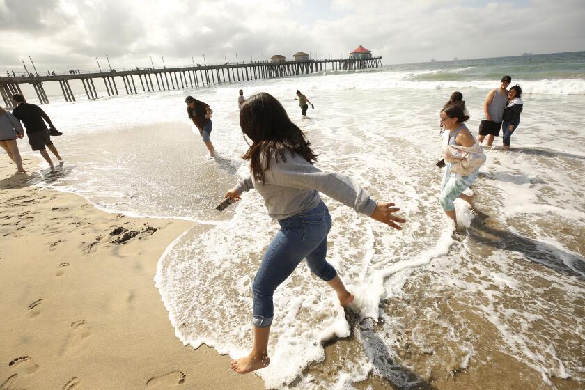 HUNTINGTON BEACH, CA - OCTOBER 11: Destiny Corrales, 14, left, and Hania Albarran, right, play in the surf as the Albarran family is visiting from Phoenix as clean-up crews continue to comb the beach at the Huntington Beach Pier after the city of Huntington Beach and California State Parks reopened city and state beaches at 6 a.m. Monday morning October 11, 2021. The joint decision to reopen the beaches comes after water-quality testing results showed non-detectable amounts of oil associated toxins in ocean water according to Huntington Beach police spokesperson Jennifer Carey. Dunn said, "The waves were not as good but it feels good to be back in the water. I feel alive!" Huntington Beach Pier on Monday, Oct. 11, 2021 in Huntington Beach, CA. (Al Seib / Los Angeles Times).