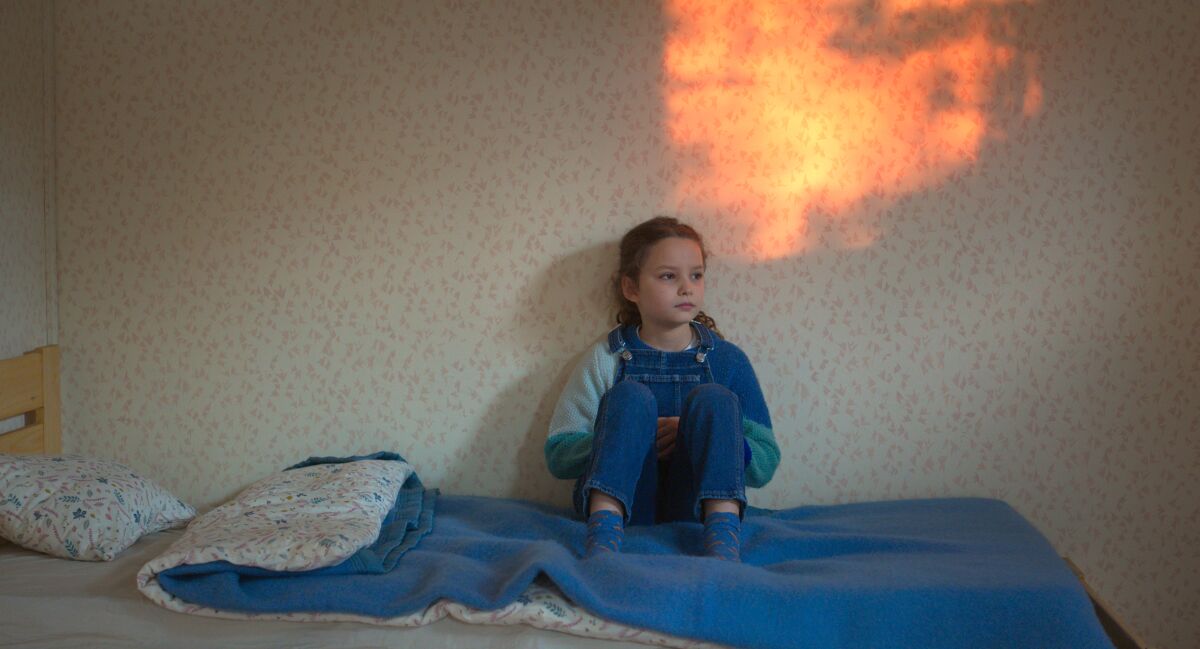 A girl sits against the wall on a bed. Light shines onto one spot on the wall 