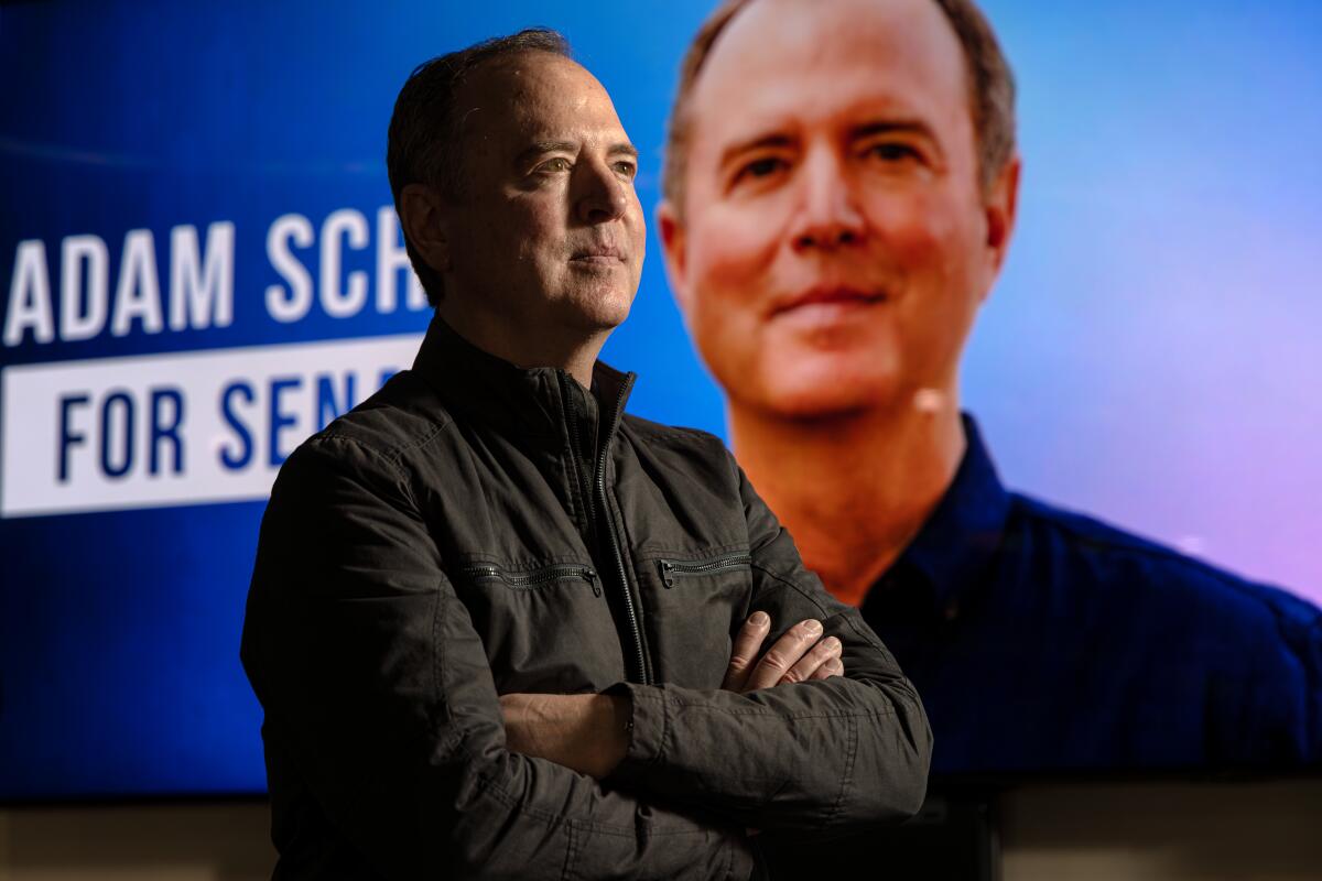 U.S. Sen.-elect Adam Schiff stands with his arms folded in front of a campaign poster.