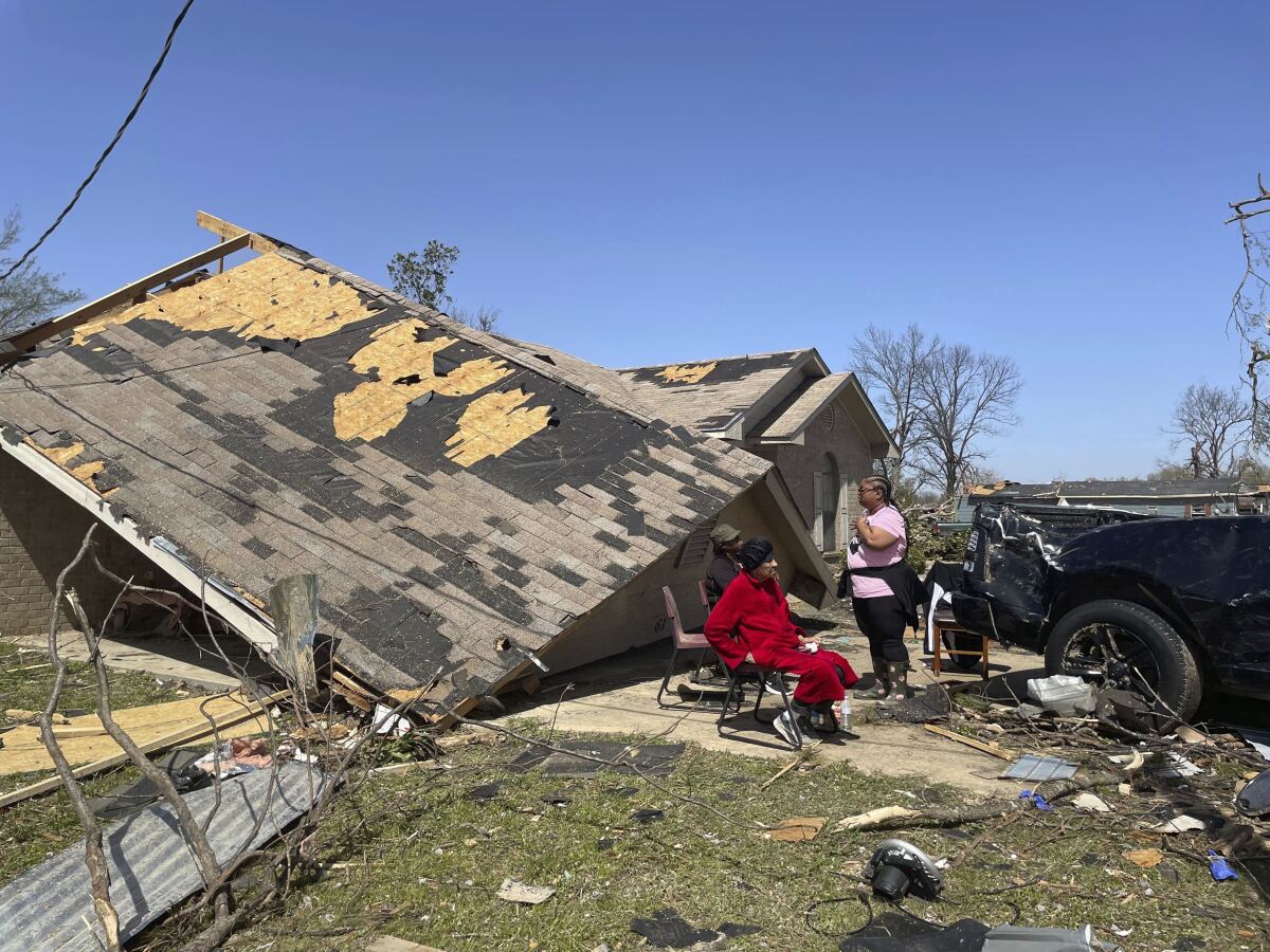 People sit in front of a damaged home on Saturday, March 25, 2023 in Silver City, Miss. Emergency officials in Mississippi say several people have been killed by tornadoes that tore through the state on Friday night, destroying buildings and knocking out power as severe weather produced hail the size of golf balls moved through several southern states. (AP Photo/Michael Goldberg)