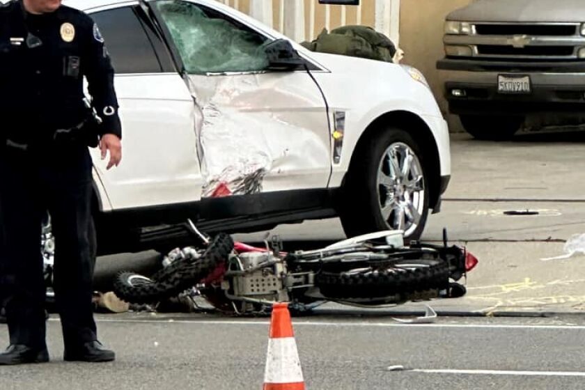 A Costa Mesa police officer inspects the scene of a crash on Placentia Avenue, during which a motorcyclist struck a vehicle.