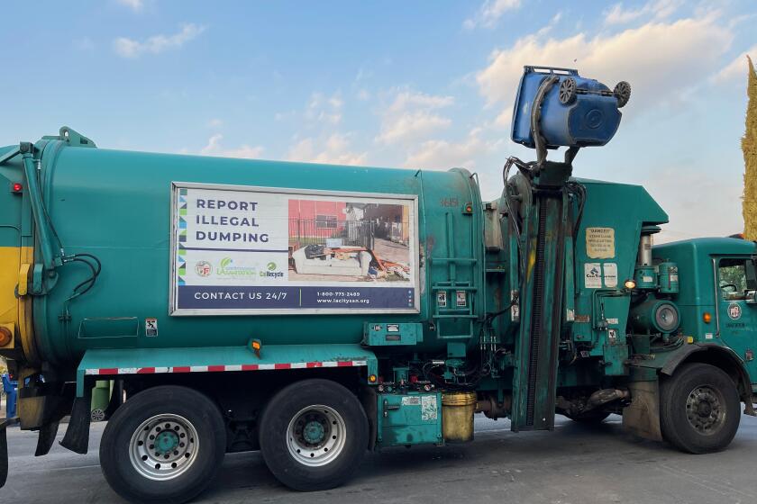 A green Los Angeles sanitation truck empties a blue recycling bin on a residential street in Highland Park on Feb. 1, 2022.