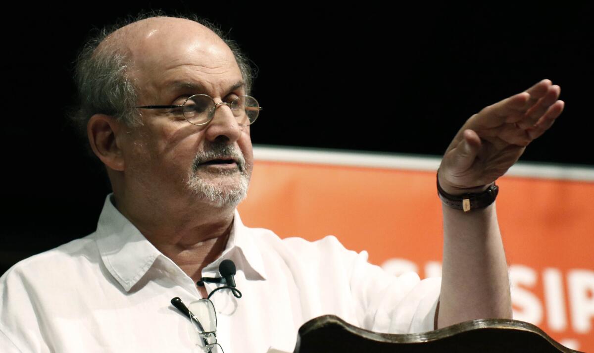 A balding man with a gray goatee and glasses gestures with his left hand while speaking