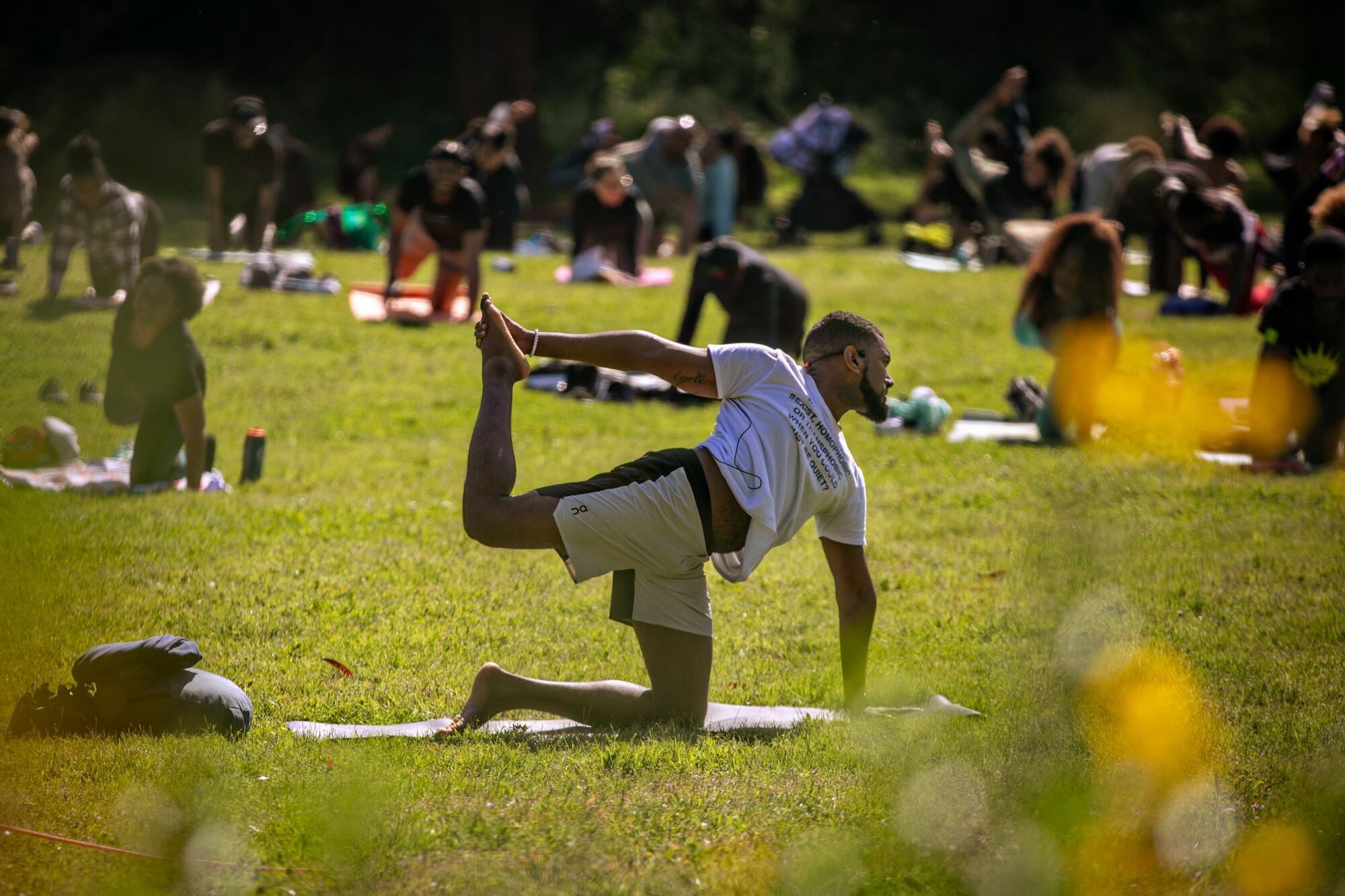 Several people are on one knee while holding up their other leg on mats on a grassy area.