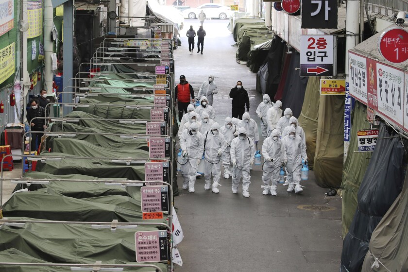 Trabajadores con ropa de protección rocían desinfectante en aerosol como precaución contra el coronavirus, en un mercado en Corea del Sur.