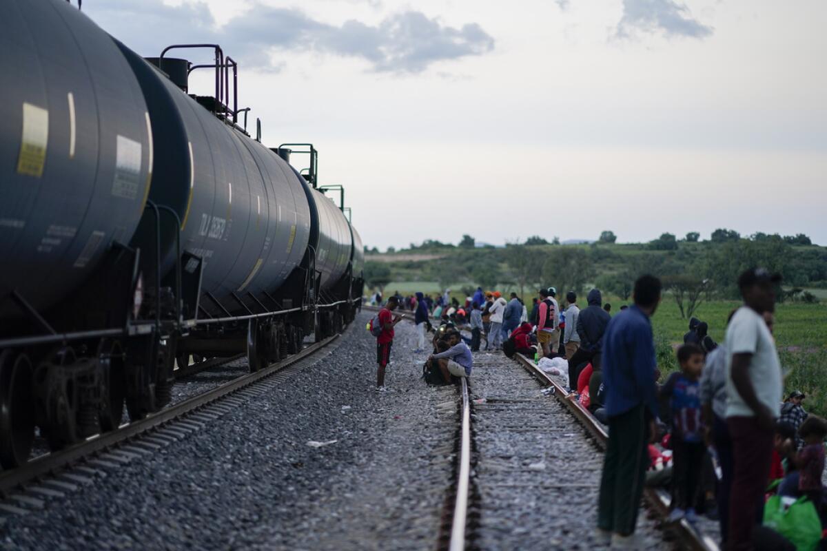 Migrantes ven pasar un tren mientras esperan a lo largo 