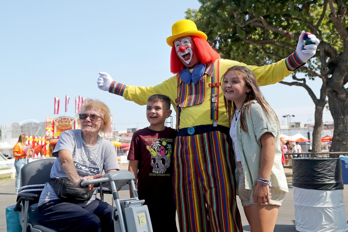 An O.C. Fair clown poses with fairgoers as they enter the main entrance during opening day, July 16, in Costa Mesa.
