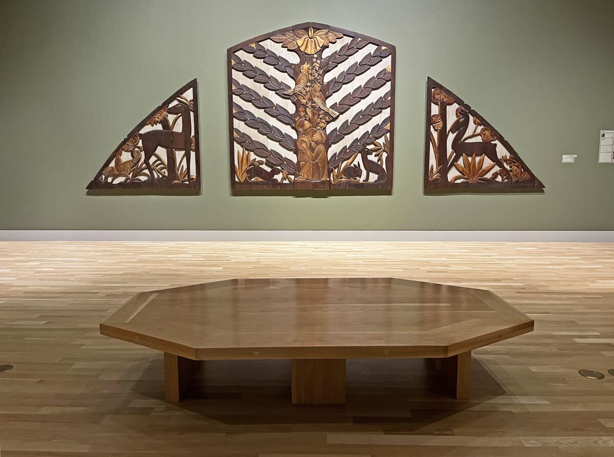 A polished hexagonal wood bench sits before a pipe organ screen carved from redwood bearing images of fauna and flora.