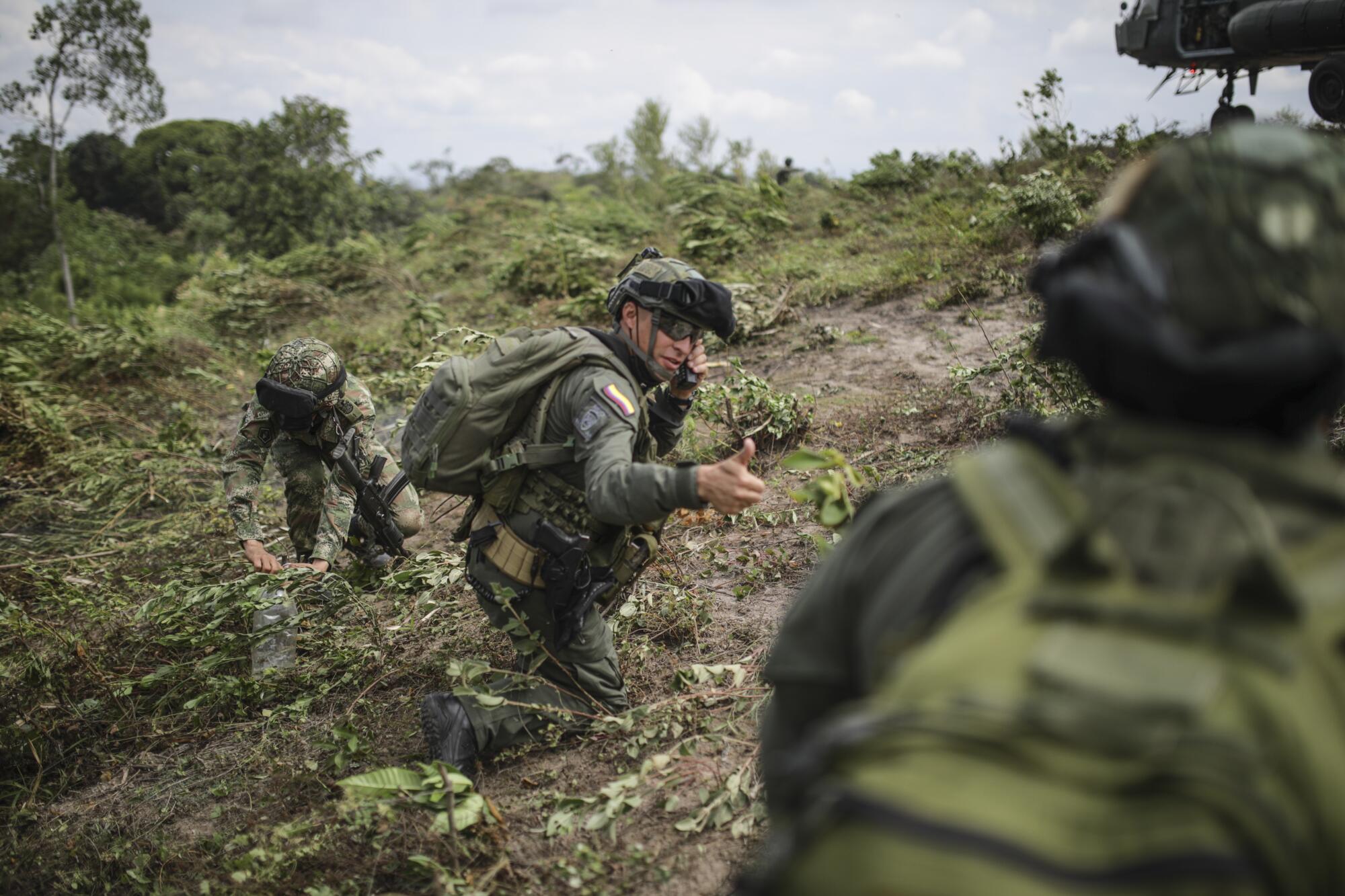 People in military fatigues on the ground amid plants.