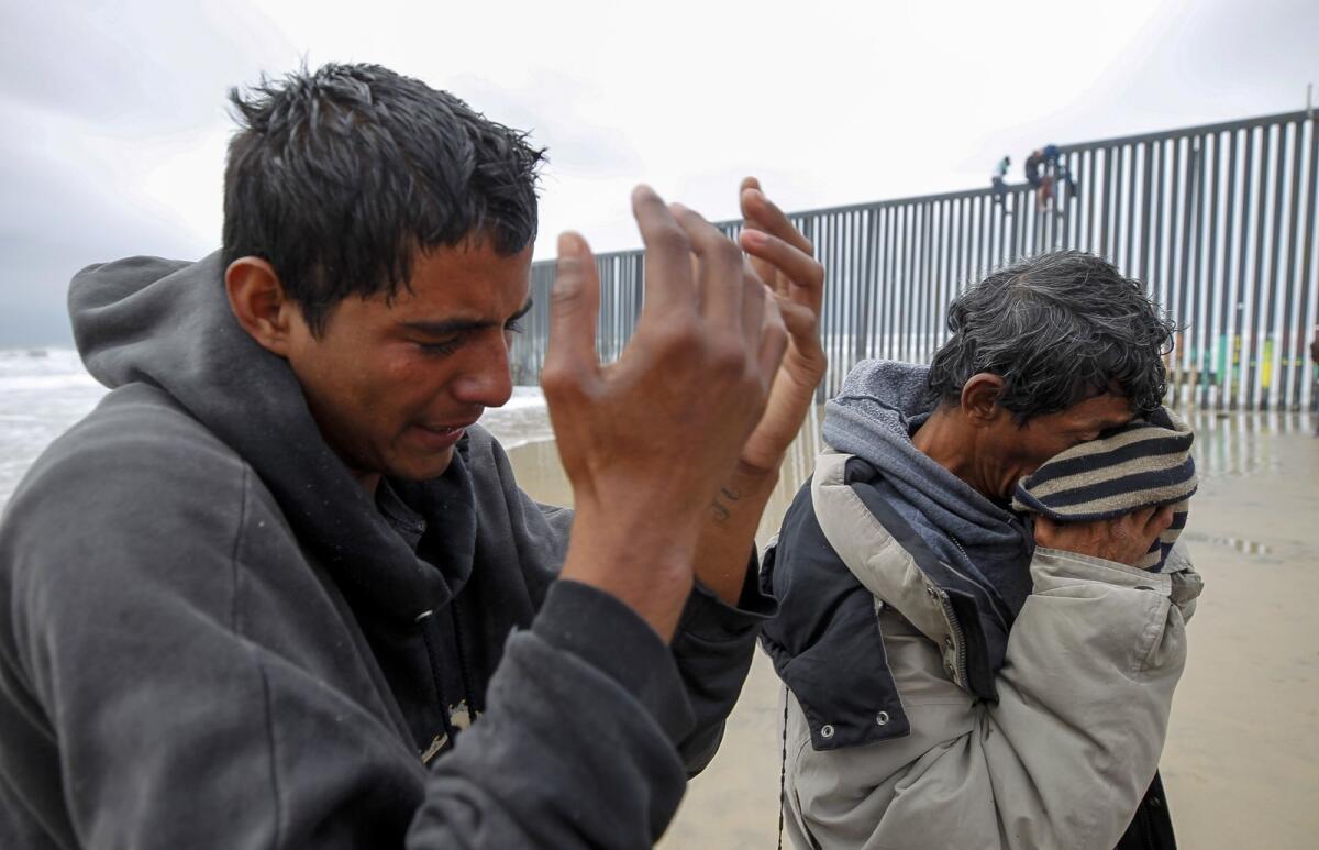 Los inmigrantes hondureños Marloh Cardona (derecha) y Gerson (quien solo dio su primer nombre) se limpian los ojos el jueves después de que los agentes estadounidenses los rociaron con pimienta en la cerca fronteriza de Playas de Tijuana.