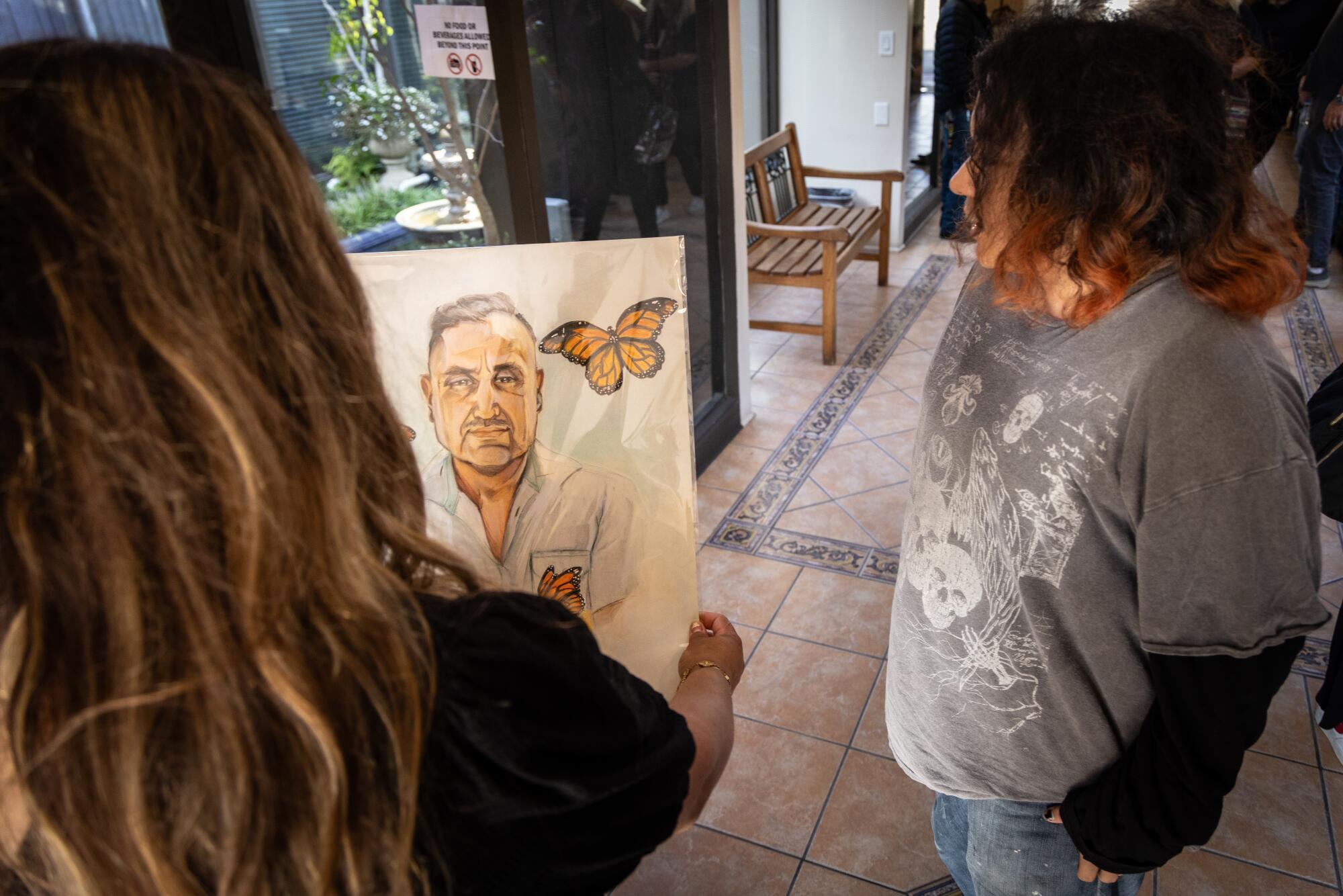 Yesenia Duran, left, the niece of of Jaime Alanis Garcia, holds a painting done by a friend.
