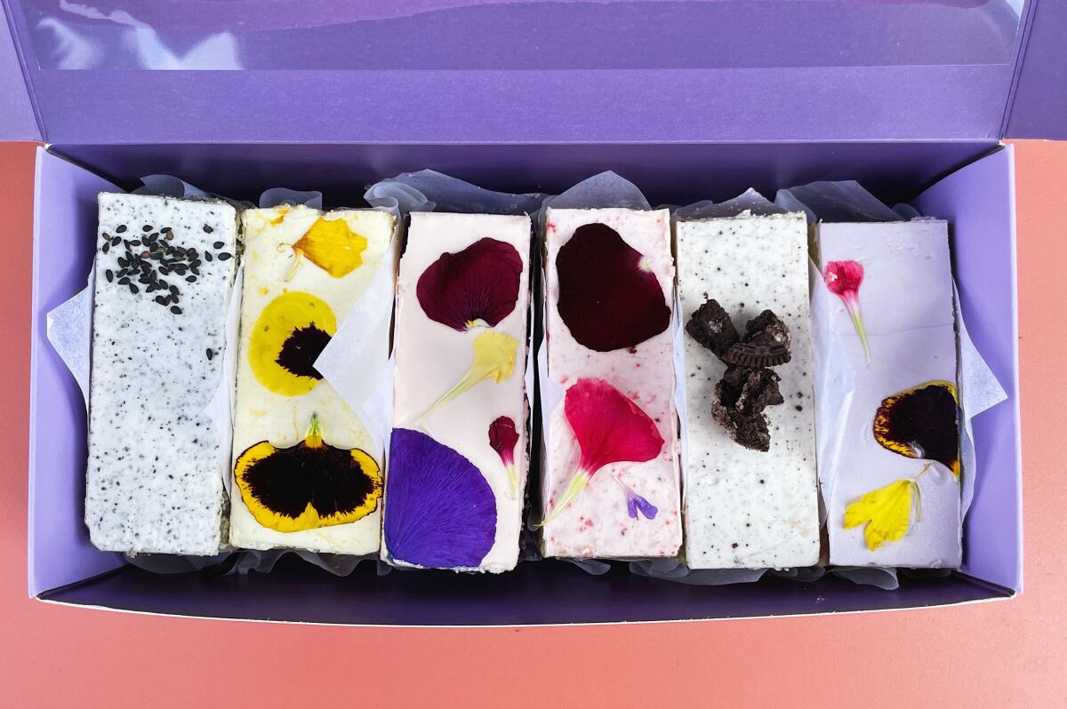 An overhead photo of a purple box of petal-topped cake bars on a pink table at Flouring in Chinatown.