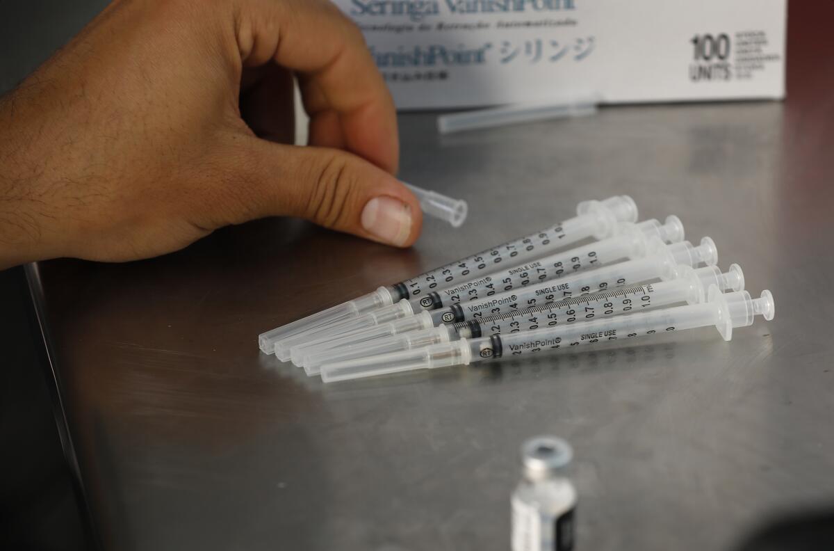 A hand reaches for an array of needles containing vaccine